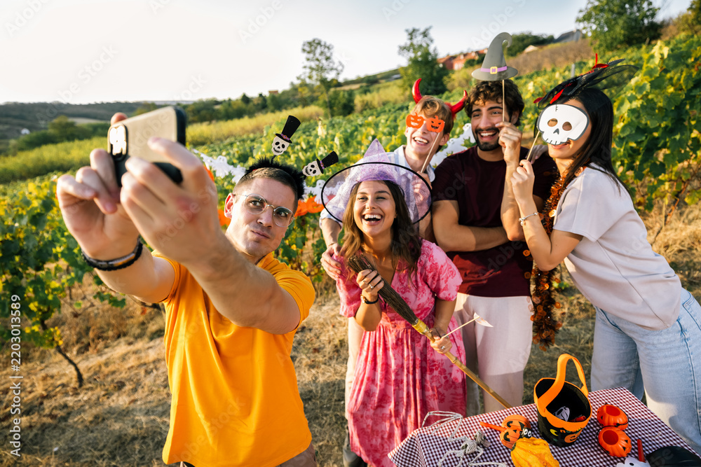 Obraz premium Young man holding a smartphone to take a group selfie with friends at a Halloween party.