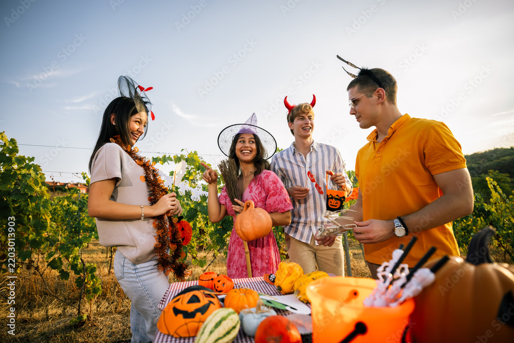 Obraz premium Friends in Halloween costumes chatting and laughing around a decorated party table outdoors.