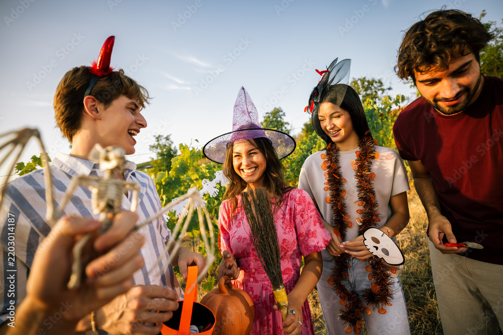 Obraz premium Young people looking at a skeleton bat prop during an outdoor Halloween celebration.