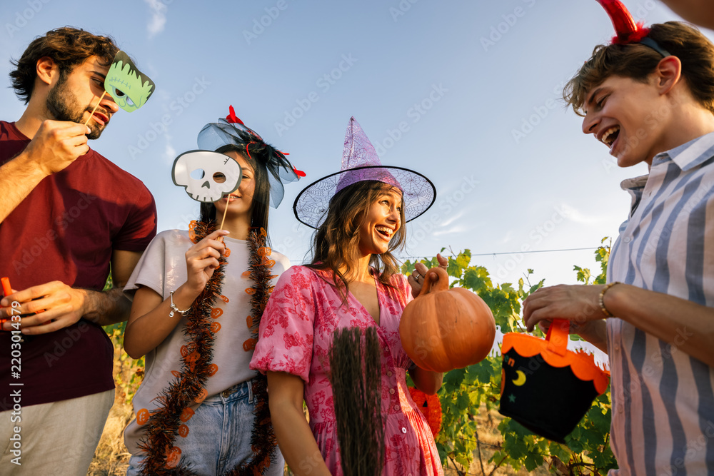 Obraz premium Young woman holding a pumpkin prop while laughing with friends at a Halloween party.