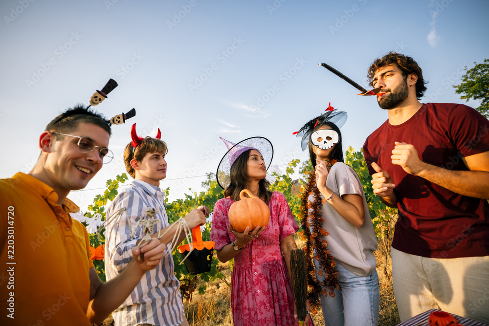 Obraz premium Group of energetic friends dancing and posing in Halloween costumes in a vineyard.