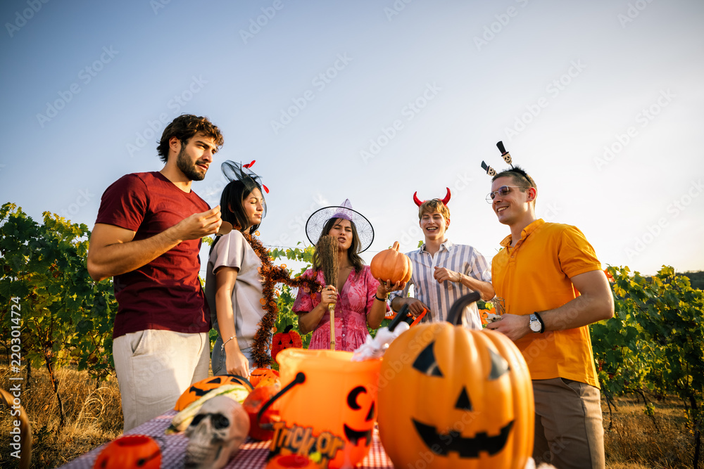 Obraz premium Group of friends celebrating Halloween outdoors around a decorated table in a vineyard.