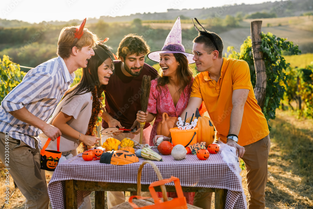Obraz premium Joyful friends leaning over a decorated Halloween table during an outdoor party.