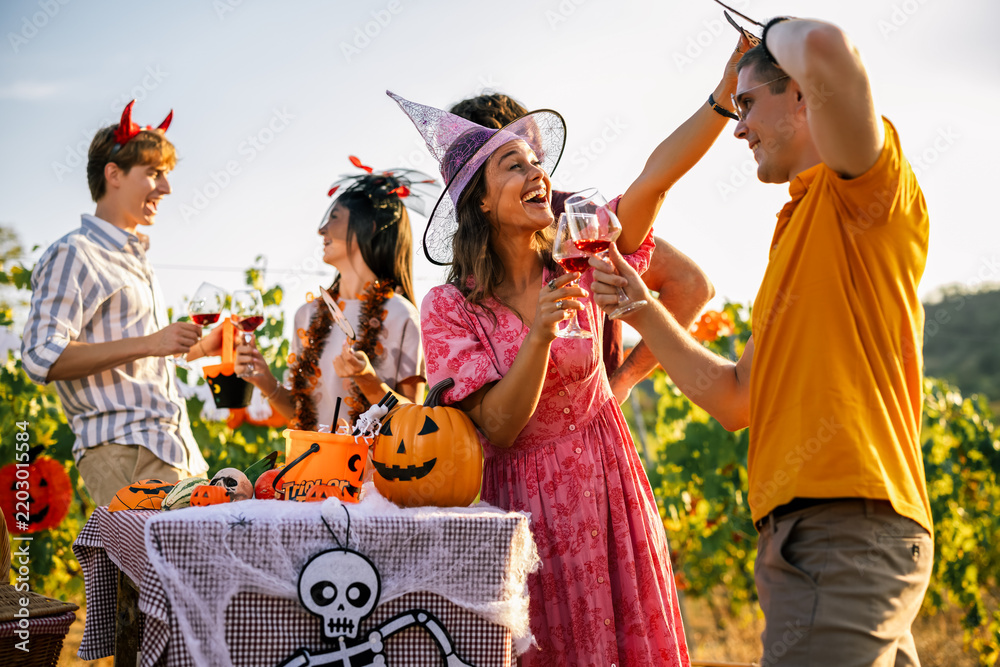 Obraz premium Group of friends cheering and drinking red wine at an outdoor Halloween celebration.