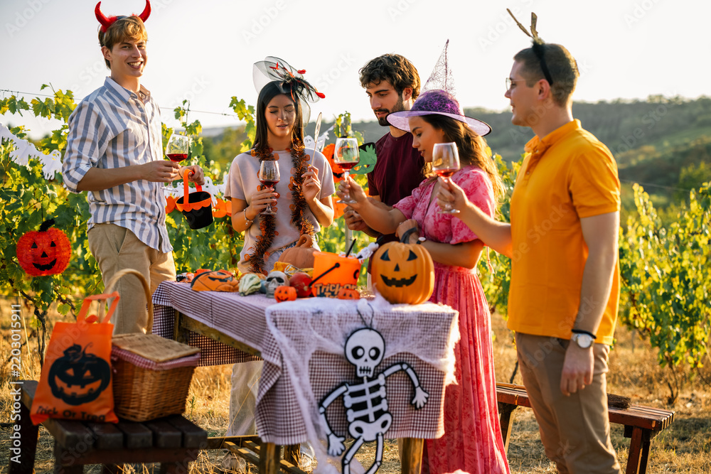 Obraz premium Friends enjoying red wine at a decorated Halloween table in a vineyard.