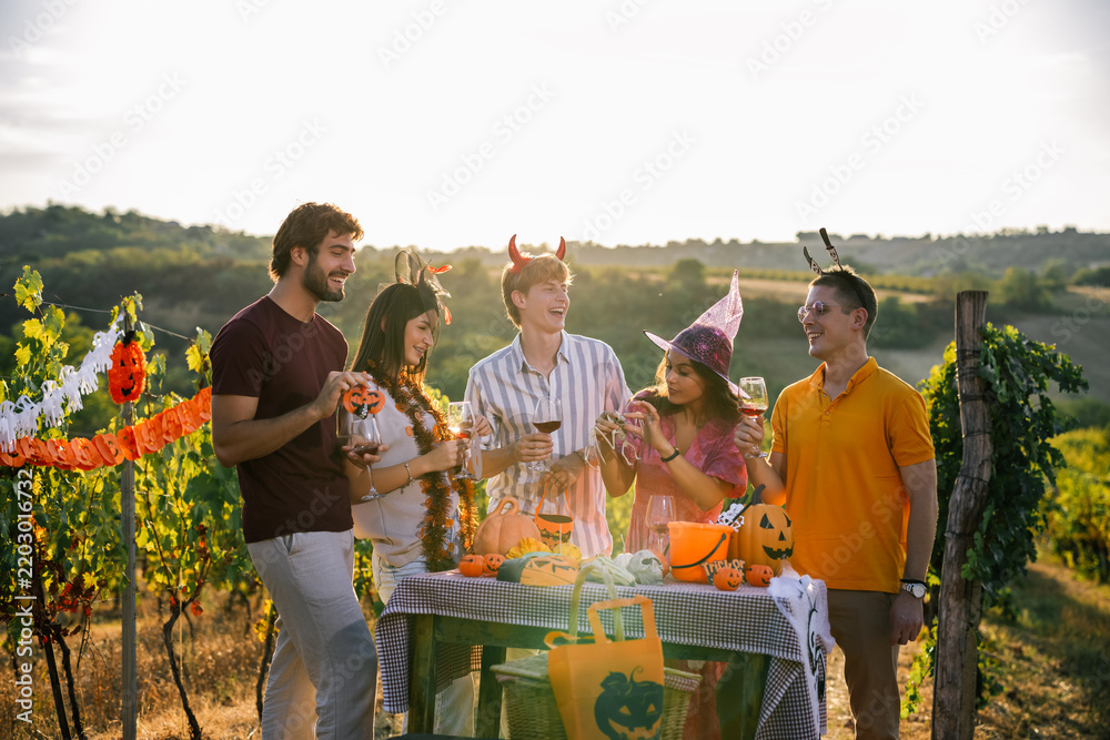 Obraz premium Group of friends talking and laughing around a Halloween-themed table set up in a sunny vineyard.