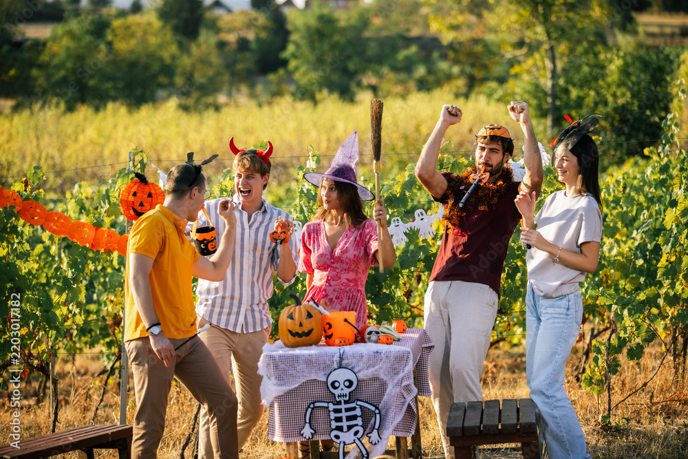 Obraz premium Five friends celebrate Halloween in a vineyard while wearing costumes and gathering around a decorated table.