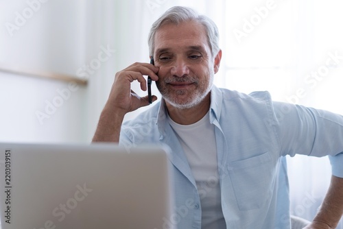 Busy mature business man talking on mobile phone in office