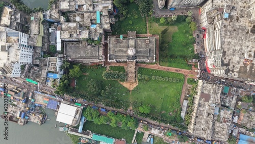 Top down aerial view of a historic building with a large green lawn and surrounding urban neighborhood near a riverbank