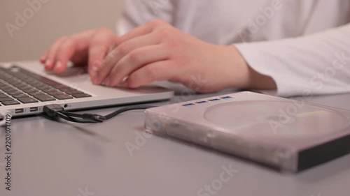 Hands carefully insert disc into drive. Closeup of disc being placed in external drive. Closeup shot showing precise placement of DVD into external USB drive with soft lighting