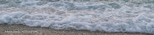 Фотография Close up view of white bubbling sea foam and wave rushing on sandy pebble beach