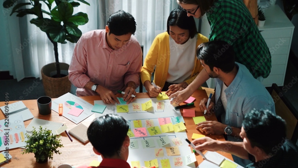 Obraz premium Close up of professional business team hands writing and putting sticky note on scrum task board. Top view of project manager write task and use kanban board to manage time and workflow. Convocation.