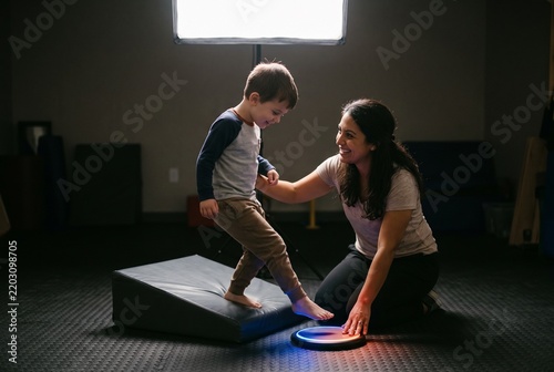 Pediatric Physical Therapist Helping Little Boy with Balance Exercises on Sensory Light Pod in Clinic