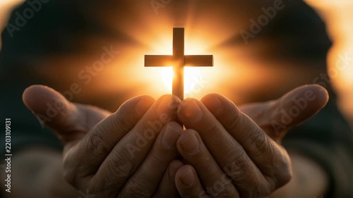 Hands hold a cross with sunlight shining behind in a clear sky
