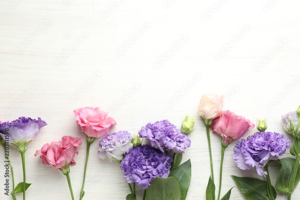Obraz premium Beautiful eustoma flowers on white wooden table, flat lay. Space for text