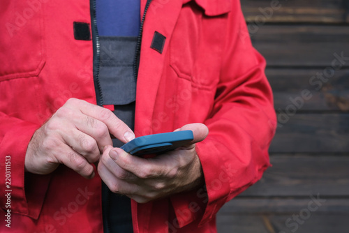 worker in red protective workwear using a smartphone outdoors, representing workplace communication, digital technology and professional activity