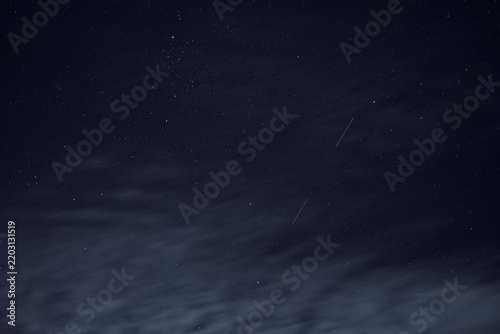 A shot of the night sky, specially processed to reduce image quality. A multitude of stars set against deep darkness, with light, translucent clouds. Faint satellite trails are visible.