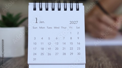 2027 calendar with person writing in a notebook in the background. Goals, planning, and resolutions concept.