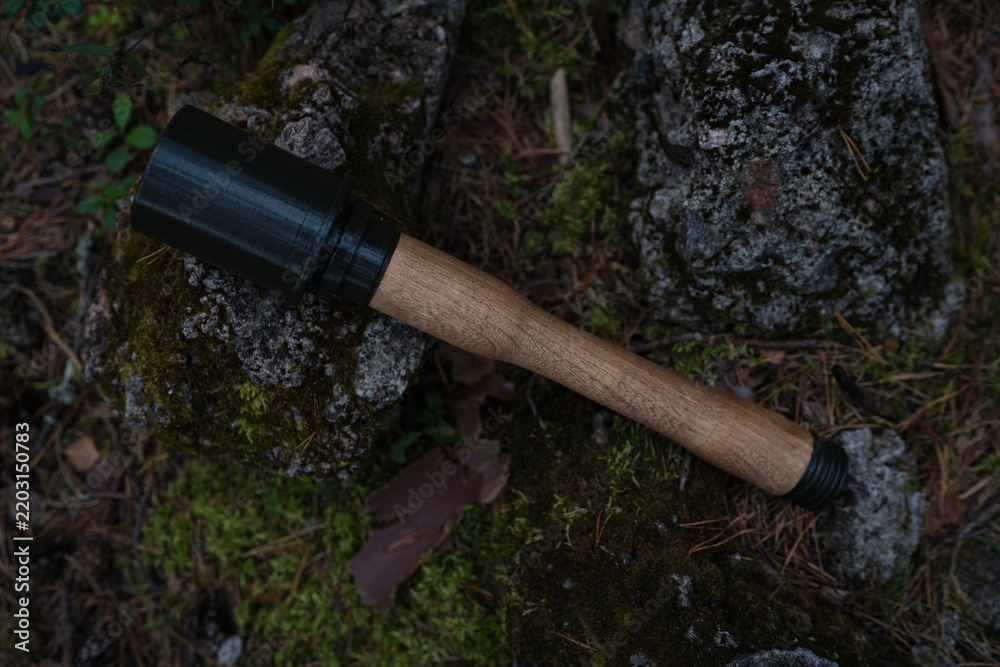 Obraz premium ​Wooden and 3D printed replica of WWII German Stielhandgranate stick grenade lying on atmospheric mossy forest ground near rocks.