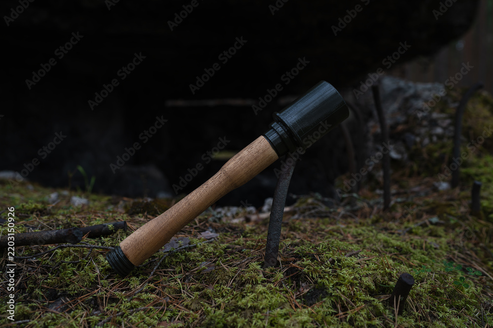 Obraz premium ​Wooden and 3D printed replica of WWII German Stielhandgranate stick grenade lying on mossy ground near a ruined old bunker.