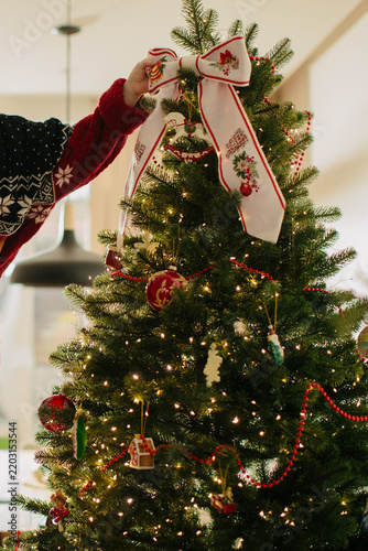 Person decorating christmas tree with ornaments and bow