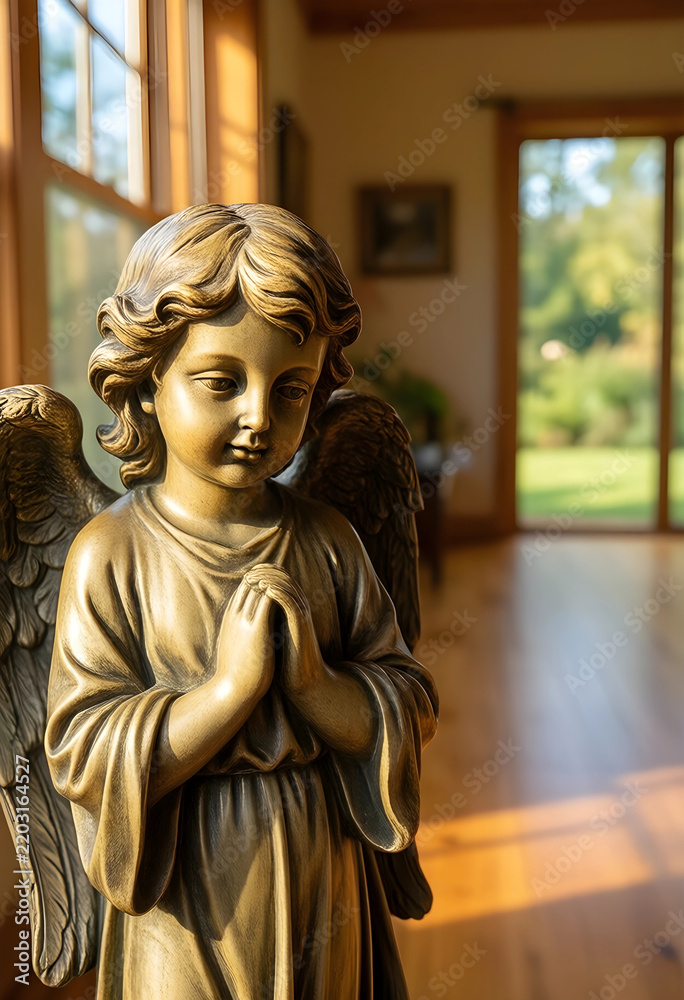 Fototapeta premium Spirituality and peace, small angel statue with hands in prayer position standing in a sunlit home interior with soft natural light and wooden floor
