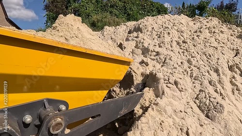 Small excavator loads itself with sand on construction site. Mini dumper transports sand close-up. Tractor loads sandy soil for construction work. Worker uses construction machinery to build house