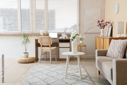 Interior of office with workplace, sofa and artificial flowers in vases