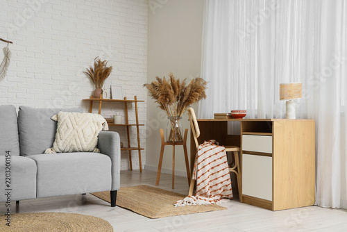 Comfortable sofa, workplace and vases with dry reeds in interior of living room