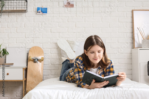 Beautiful young relaxed woman reading book and lying on bed in bedroom