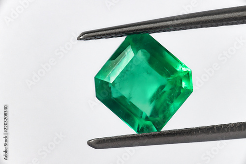 Colombian emerald cut green gemstone held in tweezers, close-up macro on white background 2