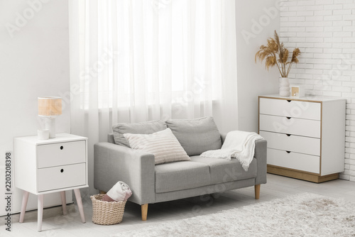 Comfortable sofa, chest of drawers and table near window in living room