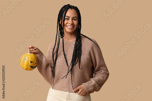 Beautiful young happy African-American woman with Halloween pumpkin on beige ...