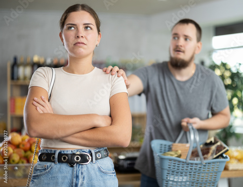 Angry girl turned away from husband during quarrel, he wants to make peace after quarrel and calms his wife, pats her on shoulder.