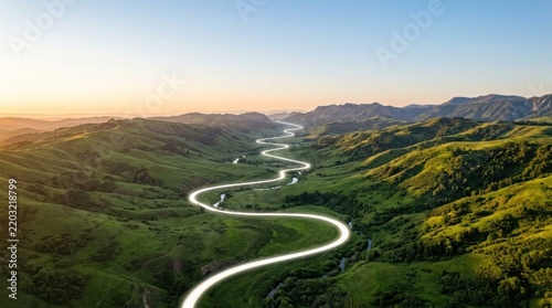 Winding road glowing light trail through green mountain valley, aerial landscape photography