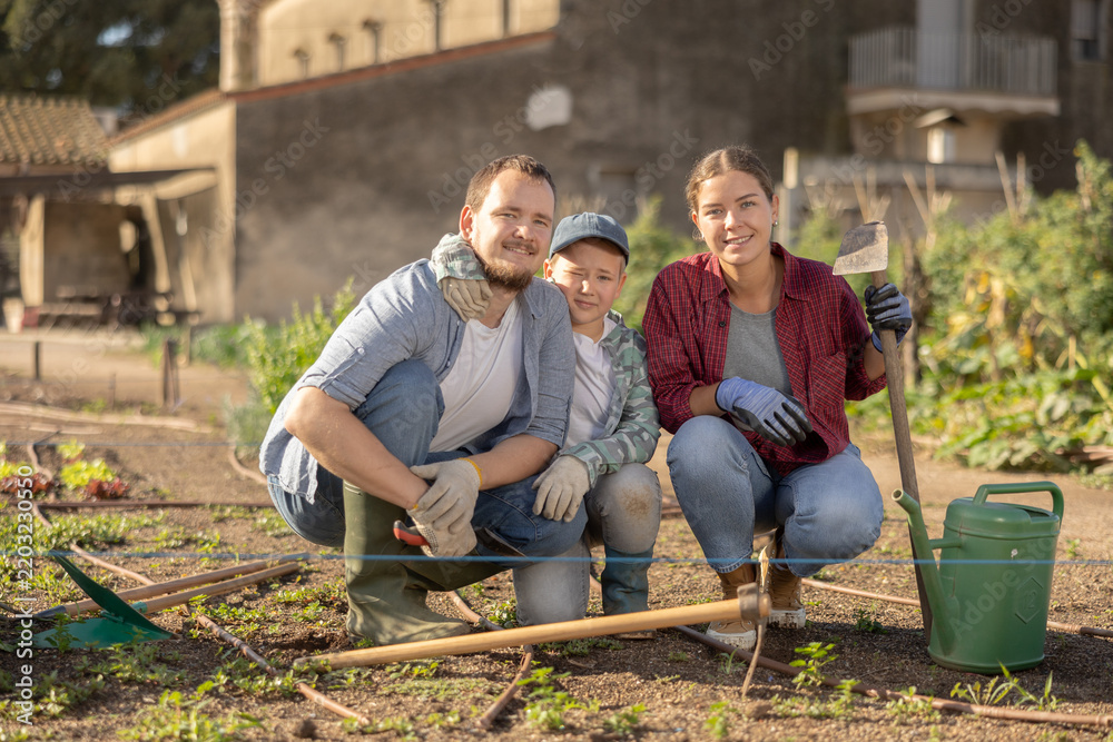Fototapeta premium Family of farmers with a watering can and a hoe in the garden after planting seeds. Farmers grow organic and organic vegetables. Portrait of a family on a farm