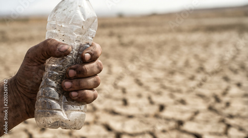 A dirty hand desperately clutches an empty plastic bottle against a desolate backdrop of severe drought and cracked earth, symbolizing the urgent global water scarcity crisis