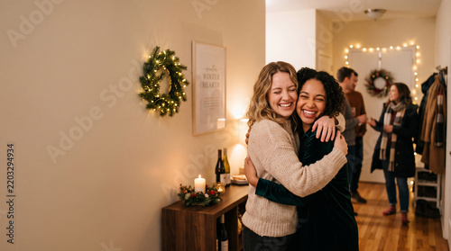 Two smiling women embracing warmly in a cozy festive hallway, soft bokeh fairy lights, ideal for holiday gatherings, seasonal parties and reunions