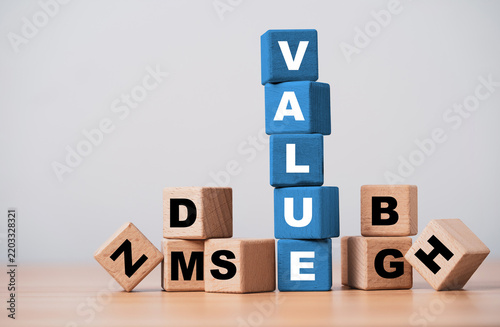 Value concept with blue wooden blocks standing above scattered letters symbolize business value, worth benefits quality, customer perception, competitive advantage and strategic value creation.