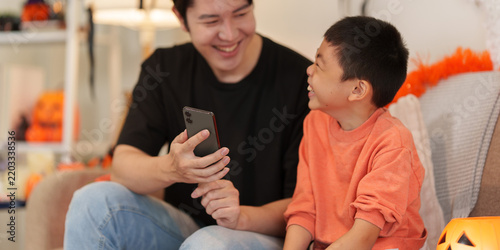 Asian father and son using smartphone together during Halloween at home