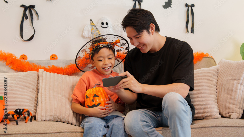 Obraz premium Asian father and son looking at smartphone together during Halloween celebration