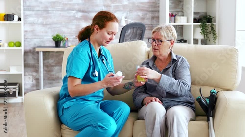 Female healthcare worker prepares medication and a drink beside a senior woman, supporting daily medication management, hydration and attentive care.