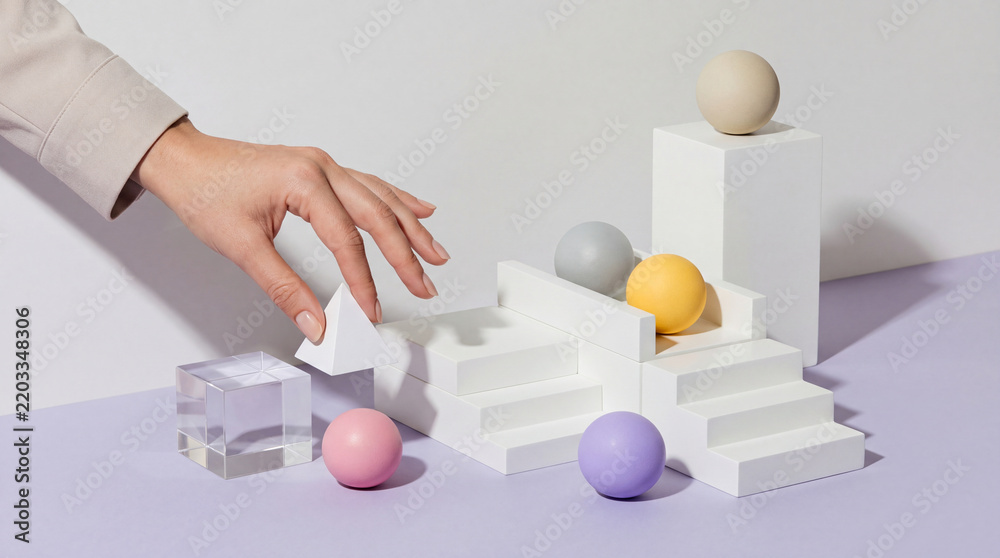 Obraz premium Female Hand Placing White Pyramid on Minimalist Geometric Stairs with Colorful Spheres and Glass Cube, Concept of Business Growth, Structural Strategy, Creative Building and Organization