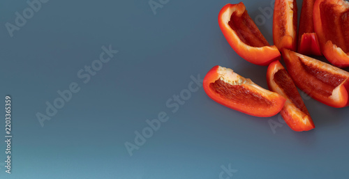 Many big paprika slices top view on grey background. Copyspace. Ripe bright red bell pepper. Simple banner template. Place for text.  Cut sweet pepper. Juicy chopped vegetable. Healthy food element