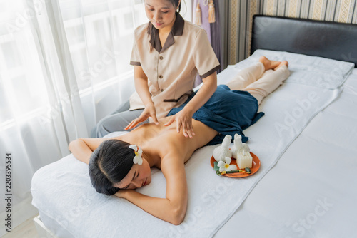 Asian woman laying on bed is being massaged by hands in room