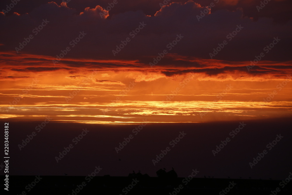 Fototapeta premium Dramatic fiery sunset with glowing orange clouds and dark sky