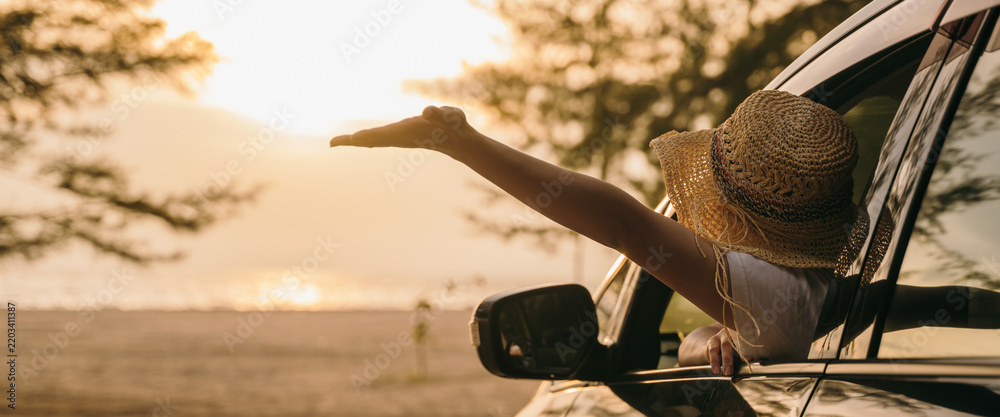Obraz premium Woman wearing straw hat sits in front seat waving hand out car window at sunset feeling the wind. Happy weekend travel enjoy summer at beach. summer vacation travel driving road trip