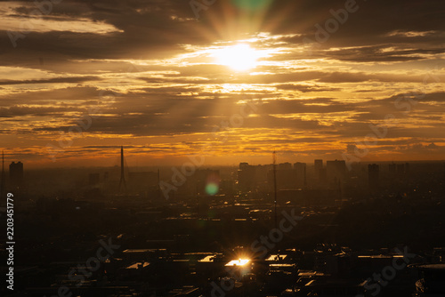 Majestic golden sunset over Bangkok city skyline silhouette with bright sun rays piercing through dramatic clouds. Urban metropolis architecture background with lens flare and copy space.