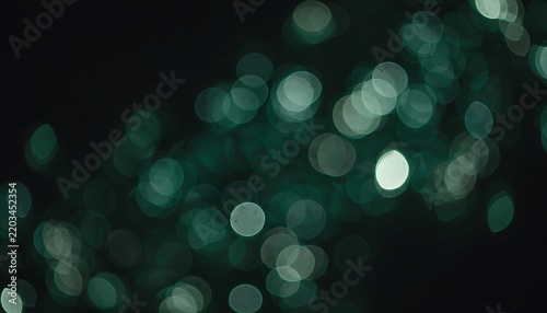 Abstract background with soft green glowing bokeh lights on a dark black surface for festive design