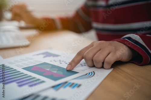 Person analyzing business chart report data with finger pointing on graph paper on wooden desk in office workspace